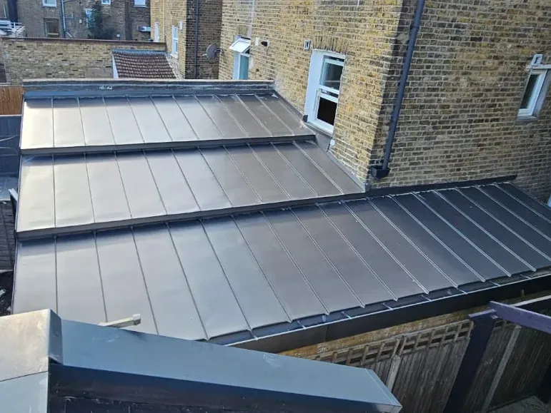 Zinc standing seam roof across stepped rear extension roofs between brick walls