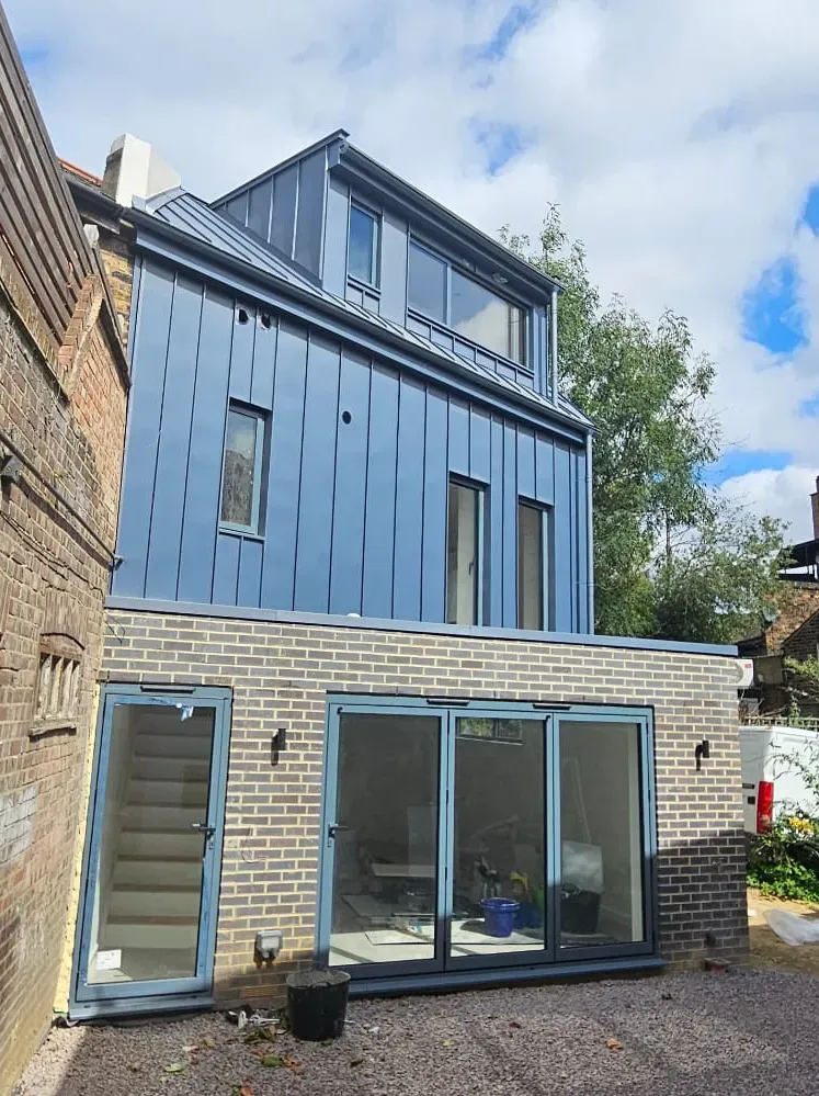 Dark zinc dormer and cladding wrapping the upper floor of a house extension