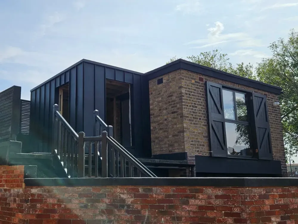 Dark aluminium-clad garden room with steps and brick retaining wall