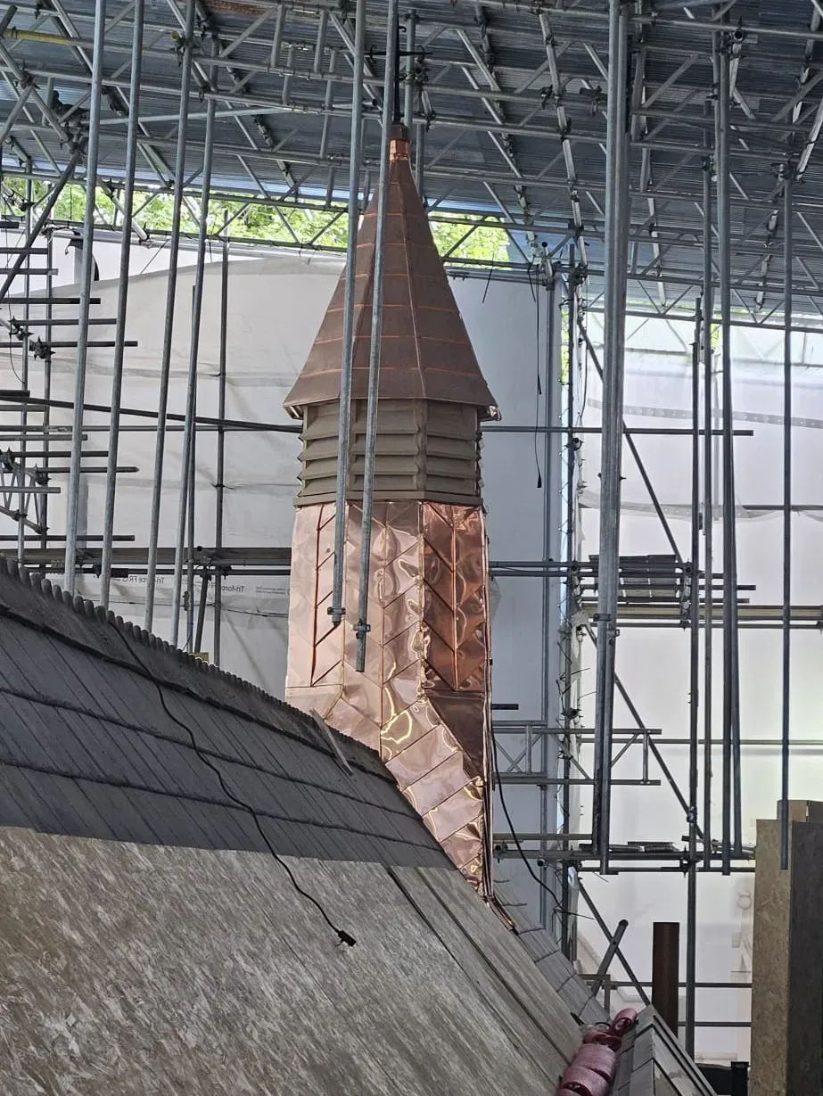 Copper-clad roof turret under construction beside a slate roof
