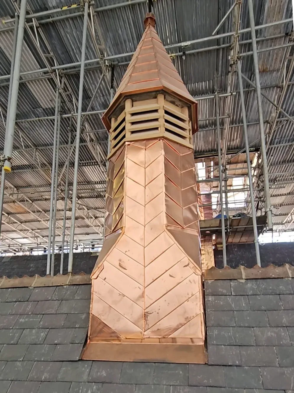 Completed copper-clad roof turret rising above a slate roof