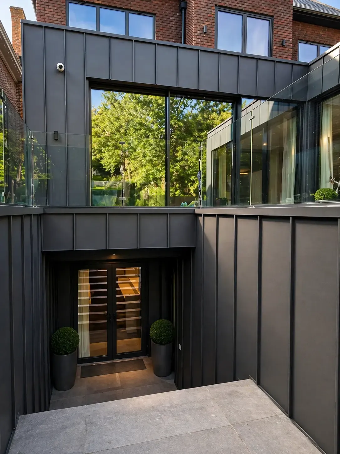 Dark steel cladding around a sunken courtyard entrance and glazed extension
