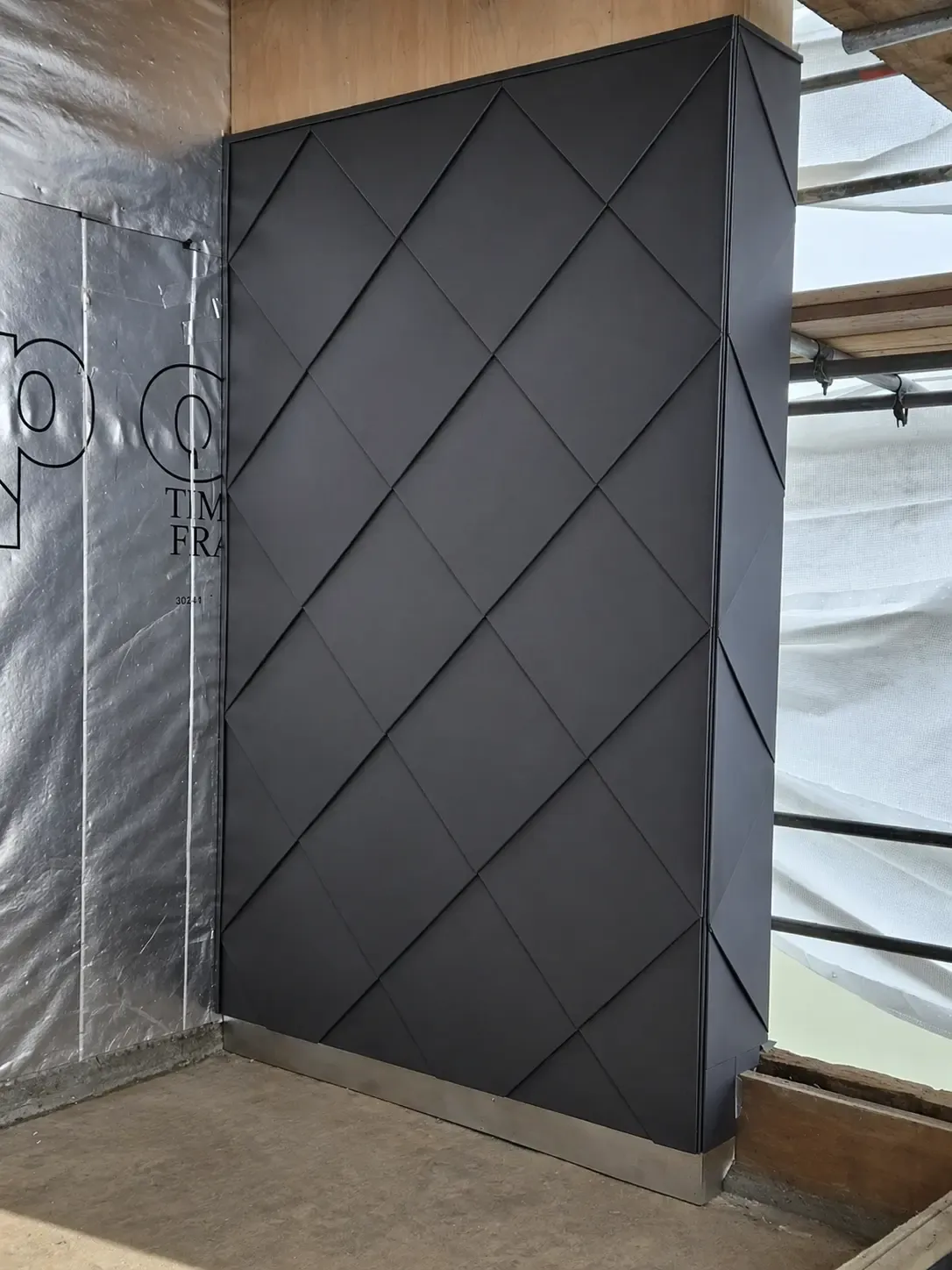 Dark steel diamond-pattern cladding detail on a wall surface