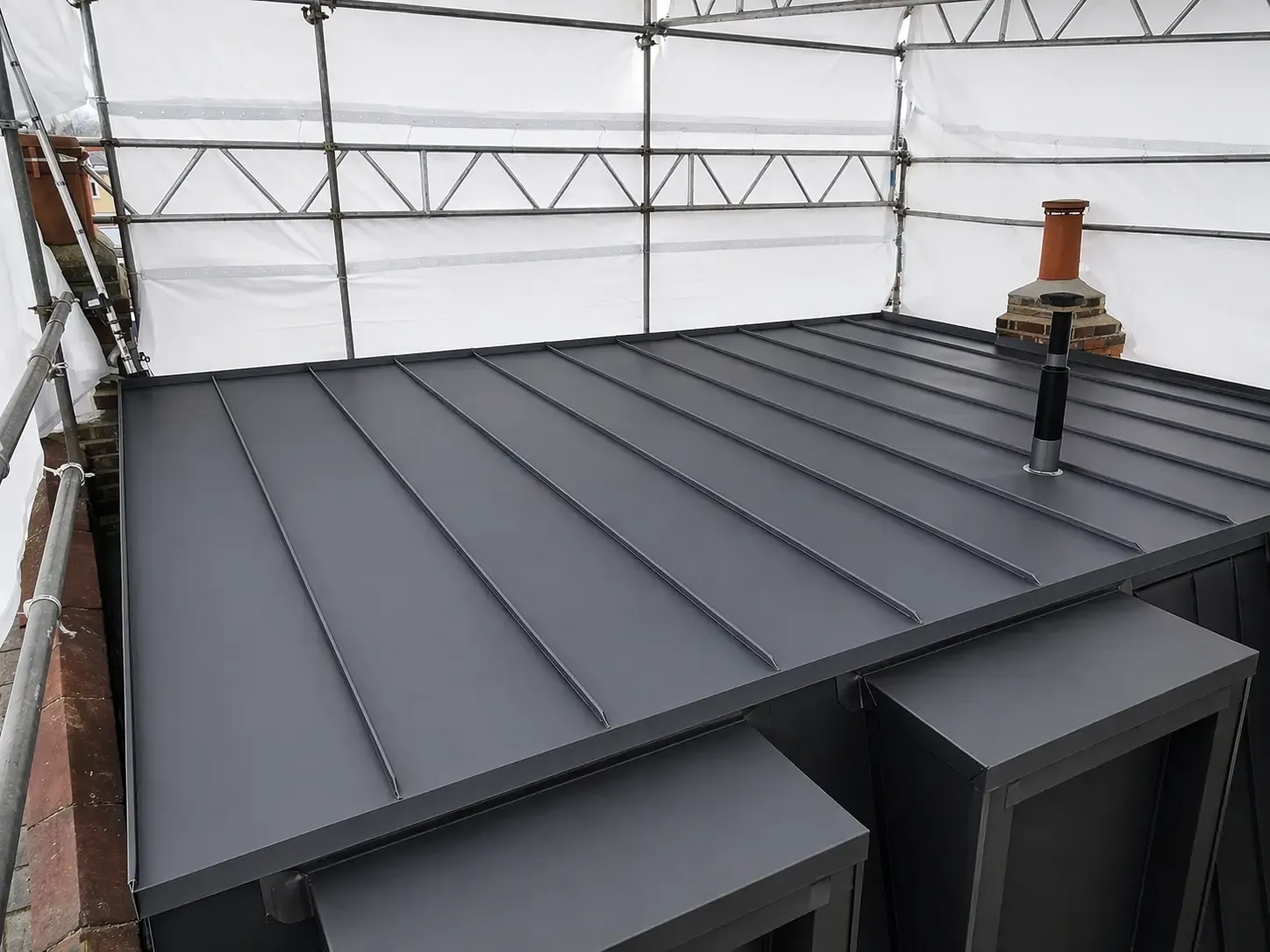 Dark zinc standing seam roof under construction with vent penetrations