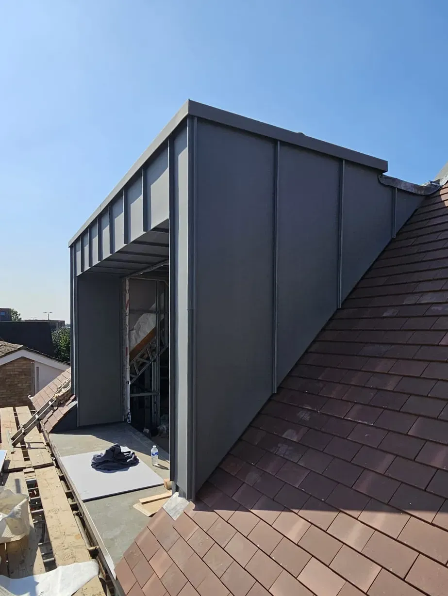 Dark zinc-clad dormer with a recessed balcony opening on a tiled roof
