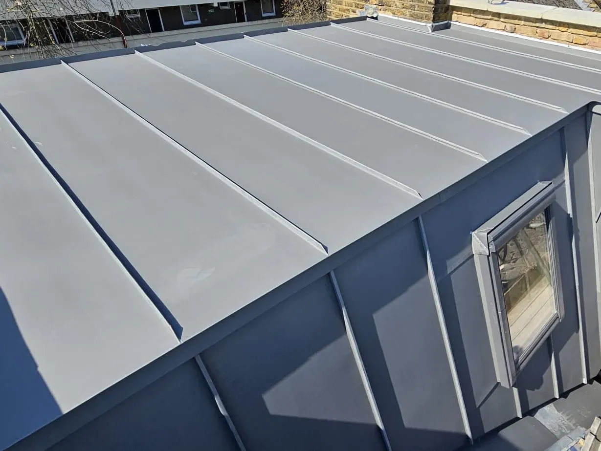 Close-up of a zinc standing seam roof with a rooflight beside blue cladding