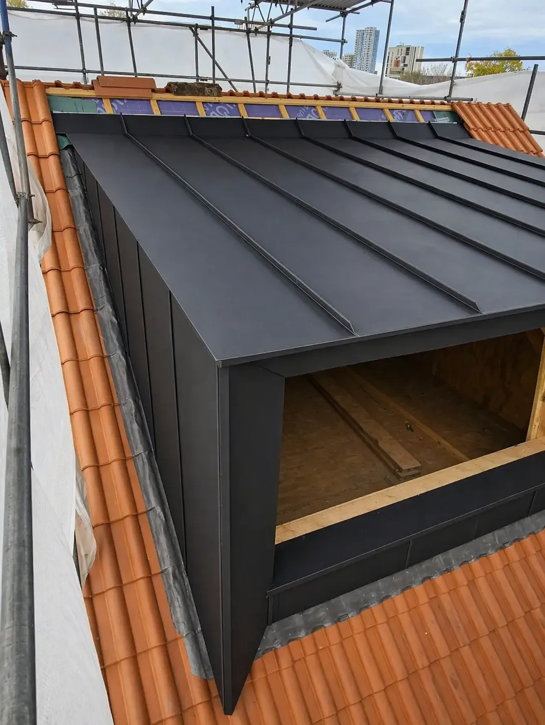Dark zinc dormer roof with large opening above a terracotta tiled roof